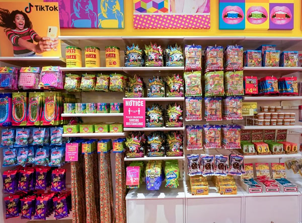 negozio fisico con scaffali ordinati e prodotti (caramelle e dolci) colorati. Quadro con ragazza che filma un tiktok in alto a sinistra