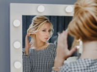 donna ripresa di spalle si aggiusta i capelli allo specchio